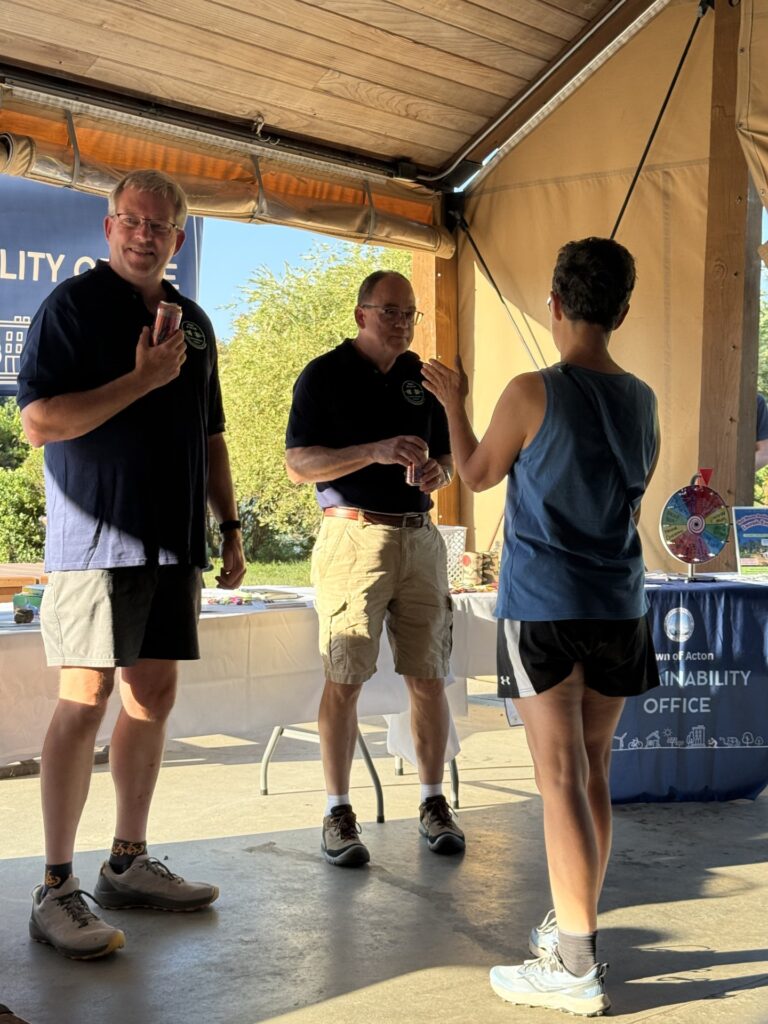 Two men in blue t-shirts talk with a woman.