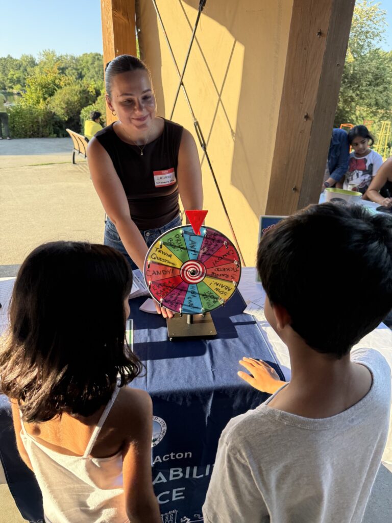 A woman spins a multi-colored wheel on a table while some kids look on.