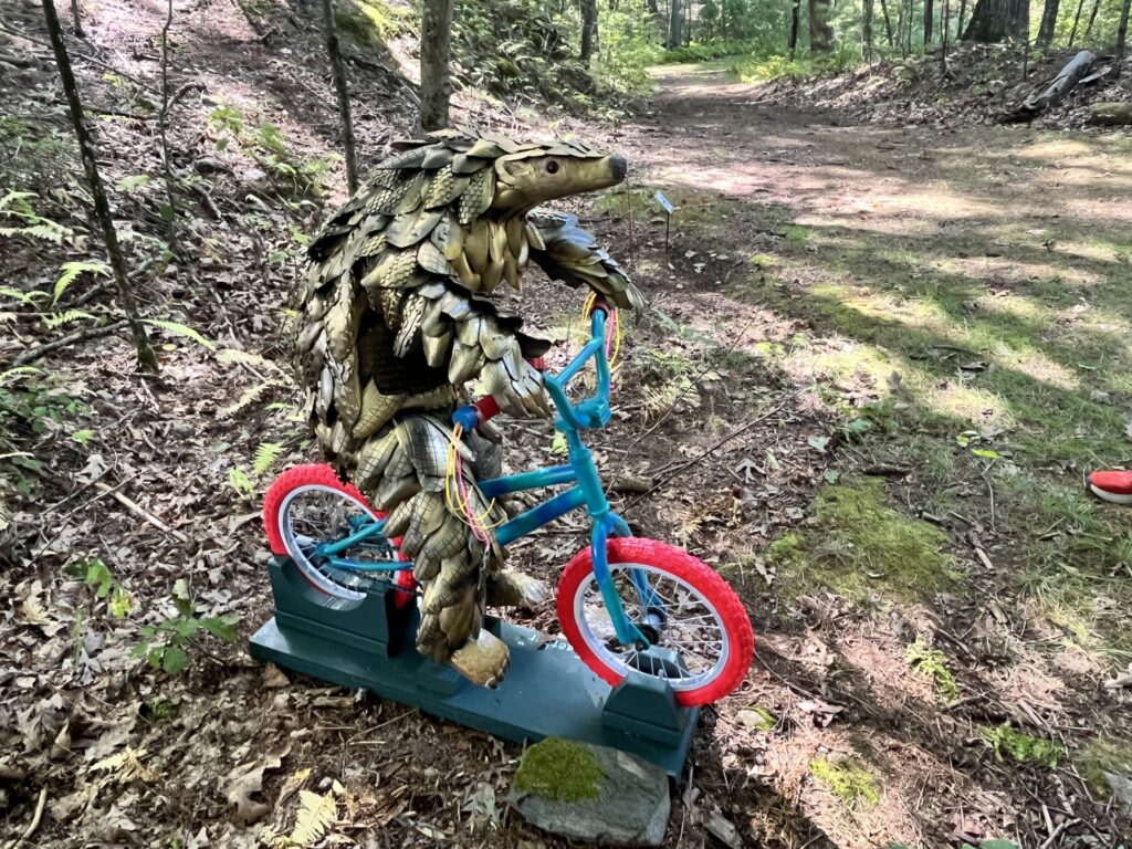 A gold-colored scaly creature riding a bright blue children's bike with bright red tires.