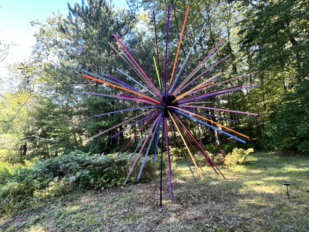 A large sculpture made out multi-colored plastic poles. The poles go out in a generally spherical pattern, looking like fireworks.