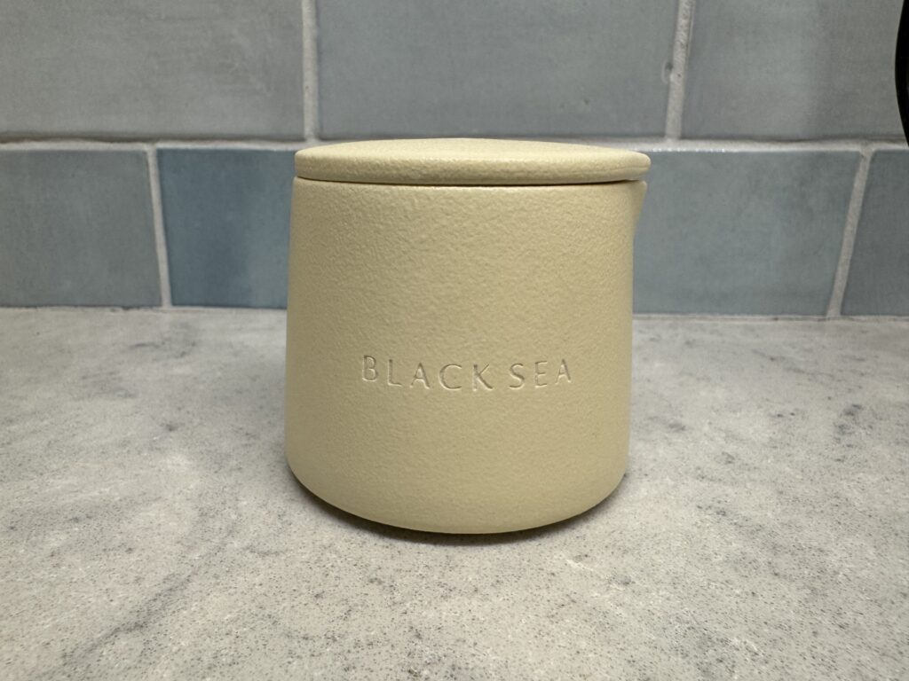 A ceramic candle, with a lid, labeled "Black Sea" sits on a table.