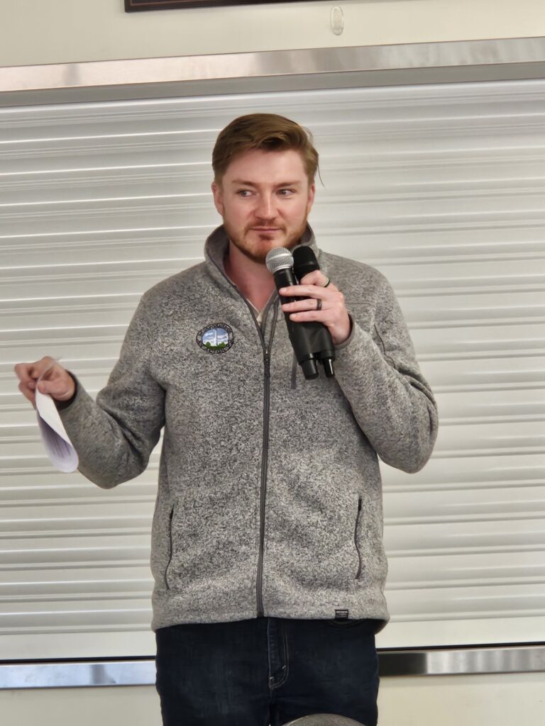 A youngish bearded man speaks to the audience.