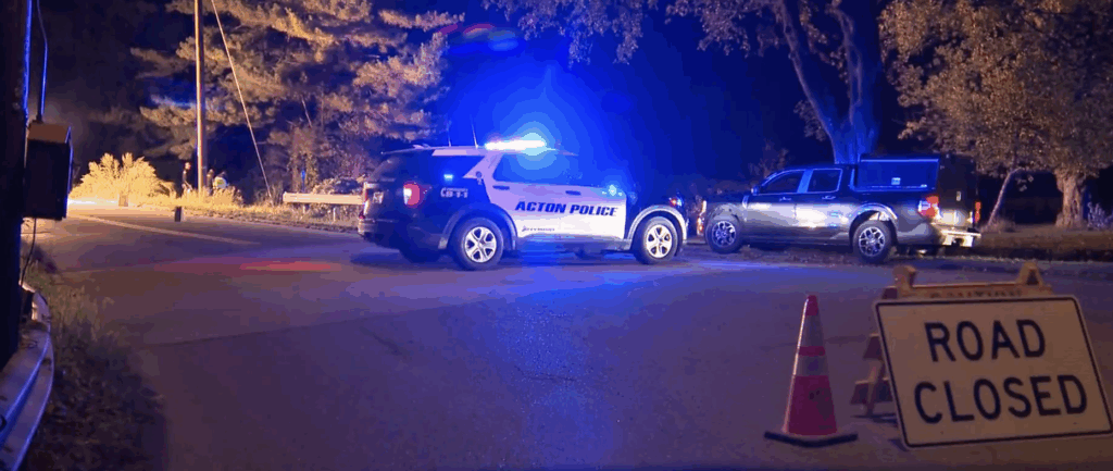Nighttime scene with Acton Police car and another black car, an orange cone, and a "road closed" sign.