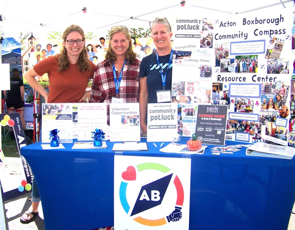 Three women stand behind a table that is filled with information about some of the services offered by the AB Community Compass.