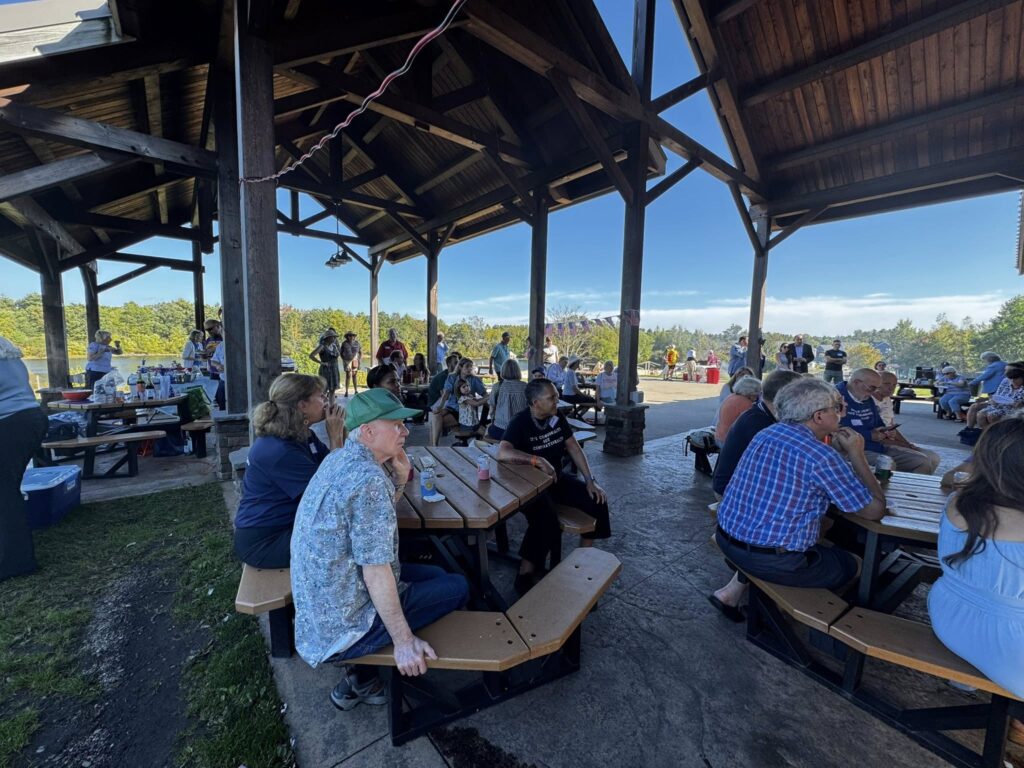 People sitting on picnic tables under a wooden canopy.