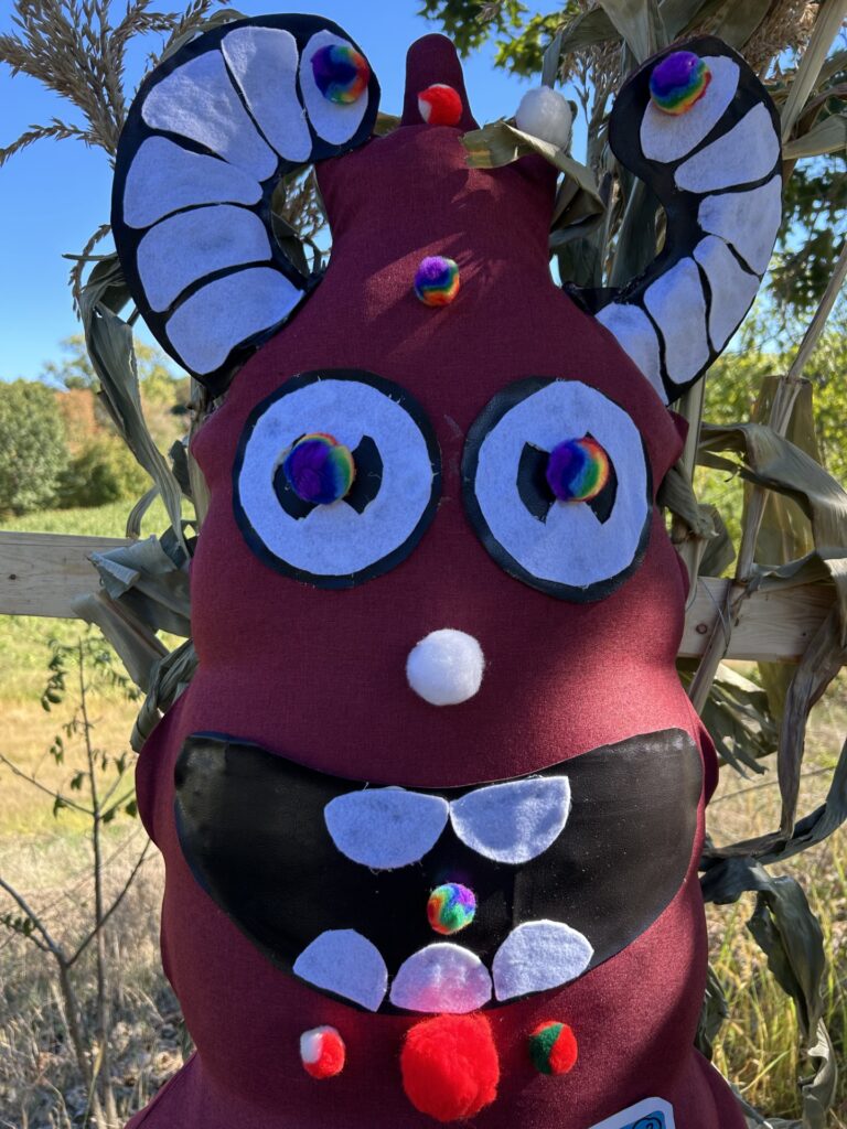 A maroon monster with black and white horns, rainbow pupils, and a pompom nose.