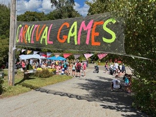 A large sign that says Carnival Games. There are people and tents in the background