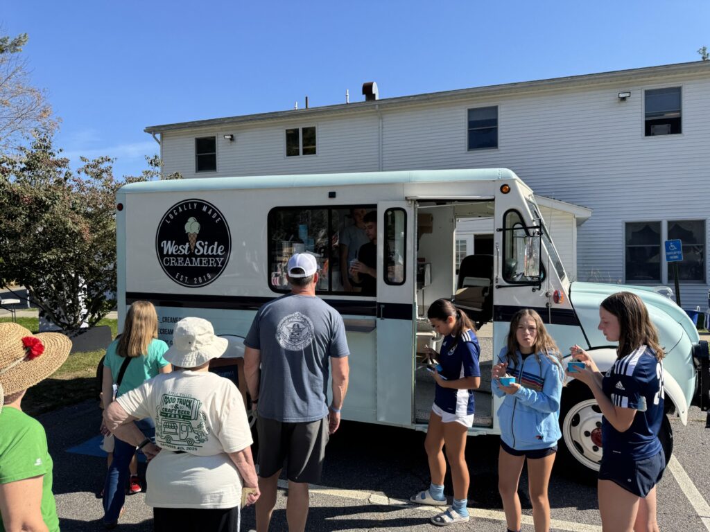 The West Side Creamery food truck has quite a line. Three teens are enjoying their purchase.