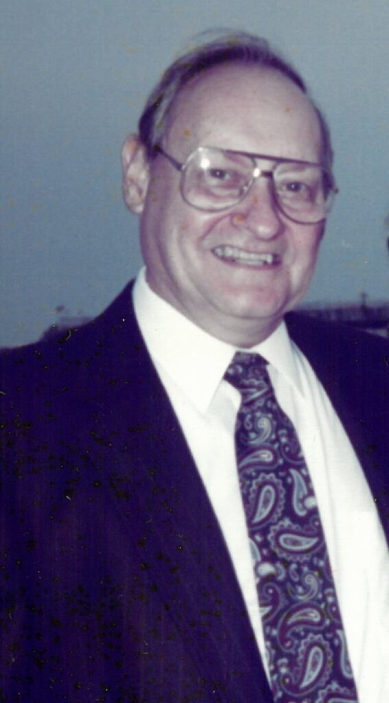 A smiling man wearing wire-frame glasses, and a suit and tie.