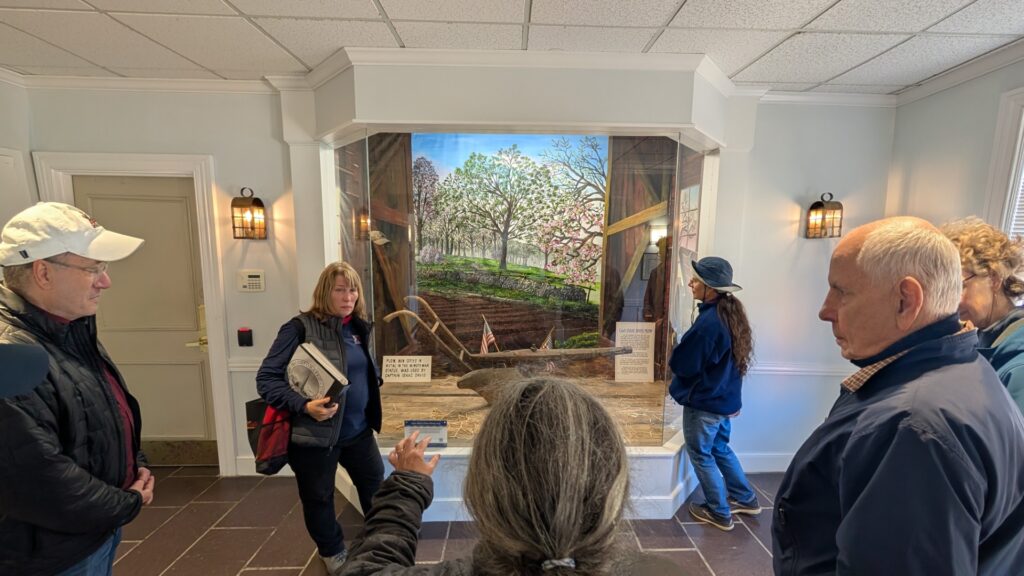 A group of people look at an old plow that is in a large glass cabinet.
