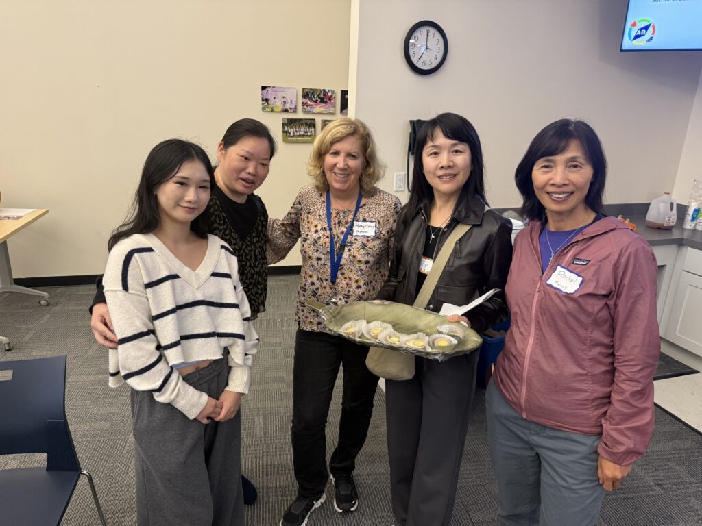 A group of five women. One holds a tray that looks to have tarts on it.