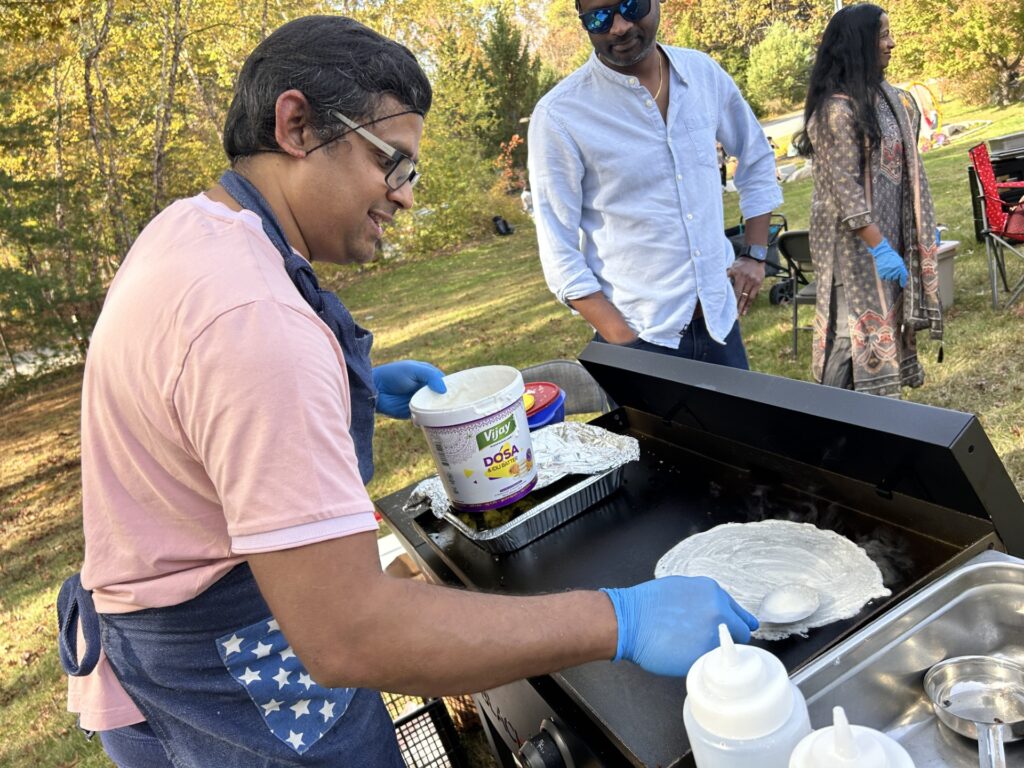 A man spreads batter on a hot grill, making a circular crepe.