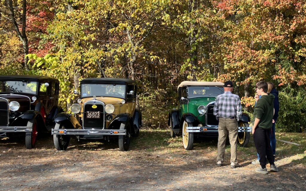 A man and a boy are checking out three very old cars lined up in the parking lot.