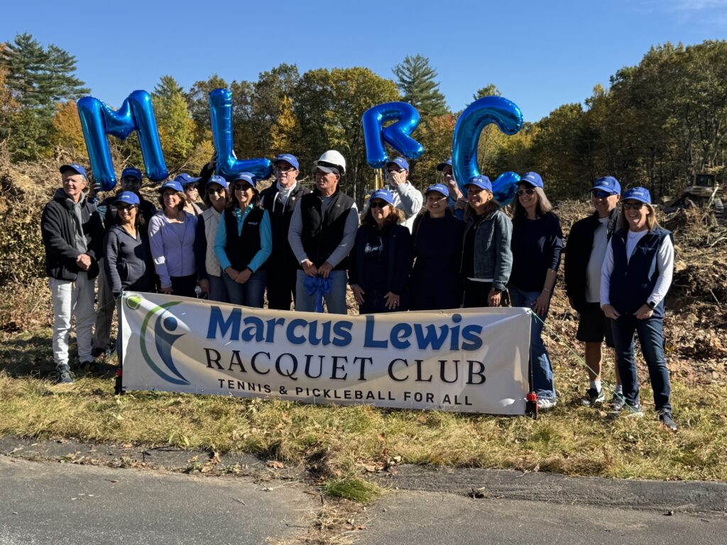 Four people sit or stand around a kitchen counter on a stage. Some of them are drinking wine.