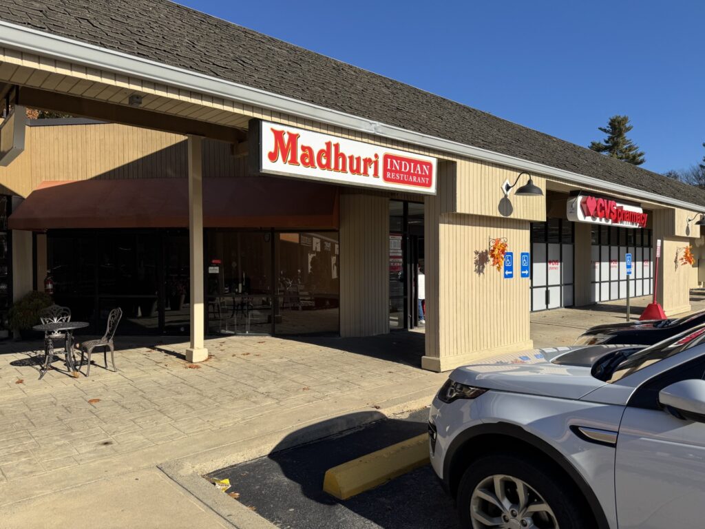 A sign for Madhuri Indian Restaurant. There are, optimistically, some tables and chairs out front.