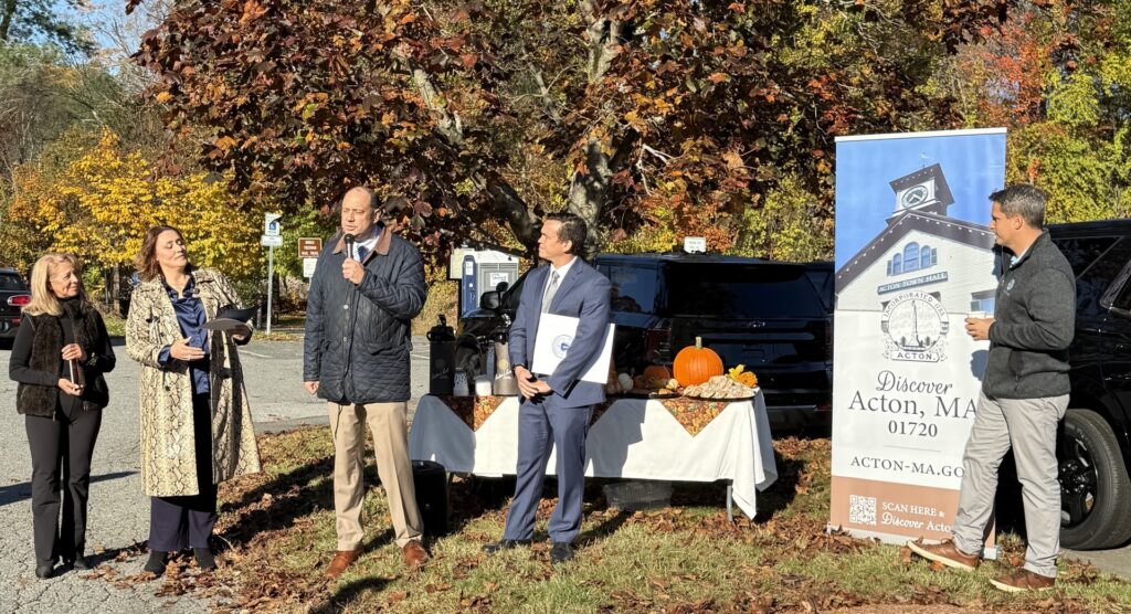 A tall man stands in front of a table with snacks. A number of other people stand watching him (including the artist, Representative Dan Sena, Town Manager John Mangiaratti, and Economic Development Director Patricia Costa).