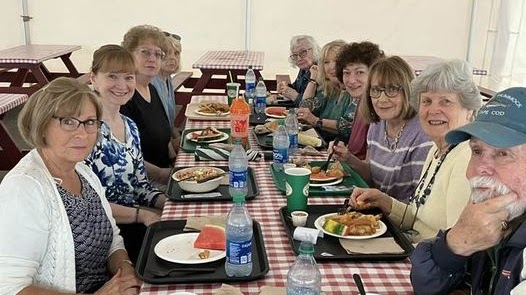 A group of women (and one man) sit at a table with a red-checkered tablecloth, They all have trays of food, as is typical from Kimball Farms.