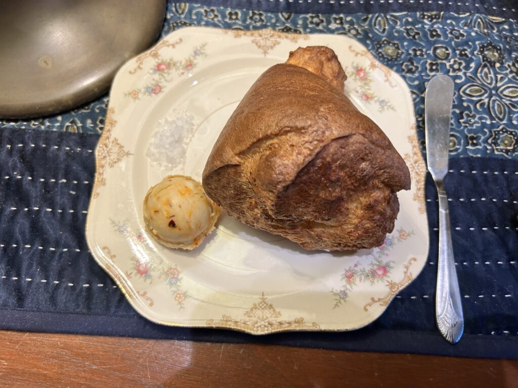 An antique dessert plate holds a large popover and a scoop of butter.