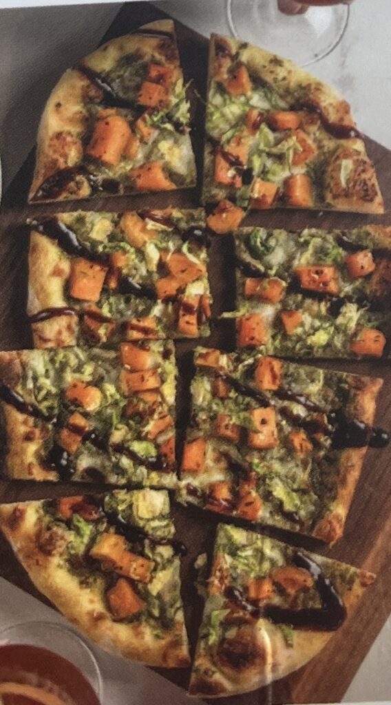 A flatbread with lots of winter squash and sliced brussels sprouts. A brown sauce decorates the whole thing. 