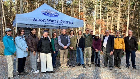 A group of people wearing walking gear stand in front of the Acton Water District tent.