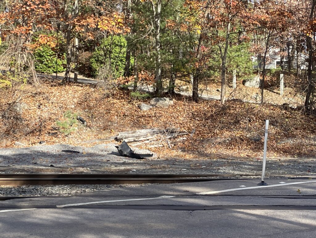 A crumpled car fender lies beside a railroad crossing.