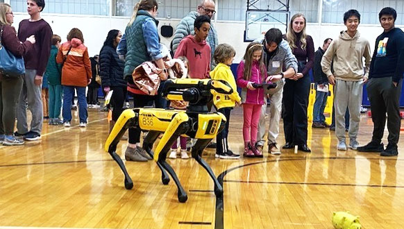 In the foreground, a yellow and black quadriped that looks vaguely dog-like, In the background, lots of kids and parents are milling around, including some who are checking out the dog.