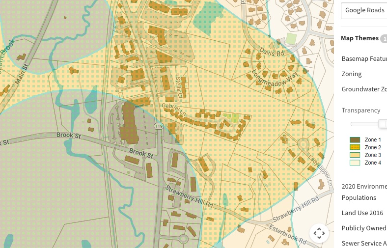 Map showing an intersection of town streets with buildings marked, overlain by shaded zones.  The legend indicates that the shadings are ground water protection zones. 