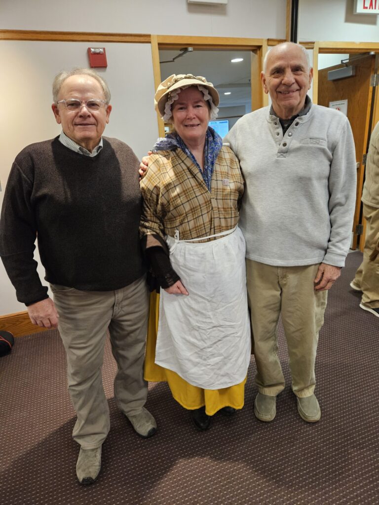 Three people in the library after the talk. The woman in the middle is wearing colonial-era dress.