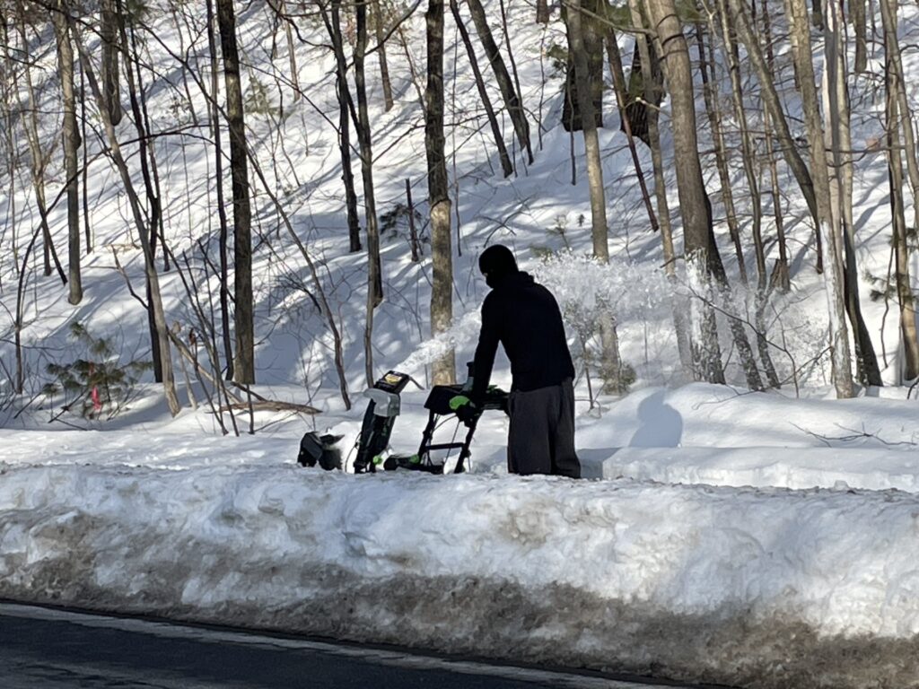 A young man pushing a snowblower on a sidewalk.