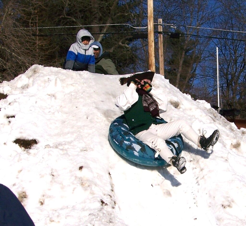 A person wearing colonial garb plays a flute while whizzing down a hill in an innertube.