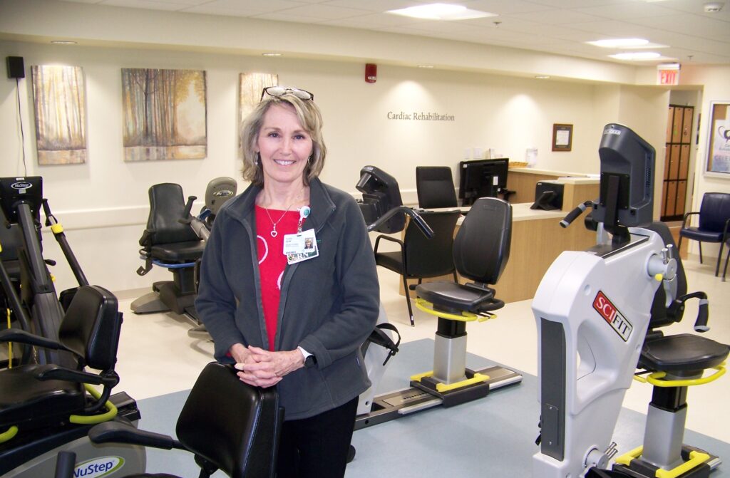 A woman wearing a red shirt and Emerson ID stands in a brightly lit room with a variety of exercise bikes.