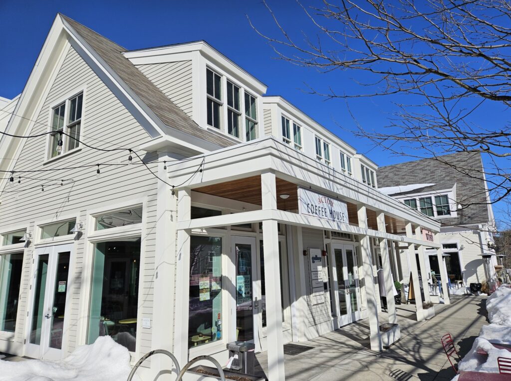 A view down a block of Mass Ave in West Acton that includes the Acton Coffee House, Wish clothing store, and True West Brewery in the distance.