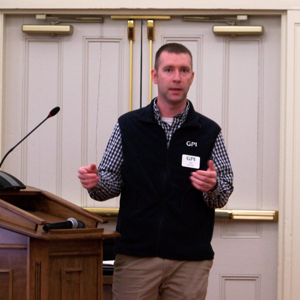 A man wearing a GPI vest speaks to an audience.