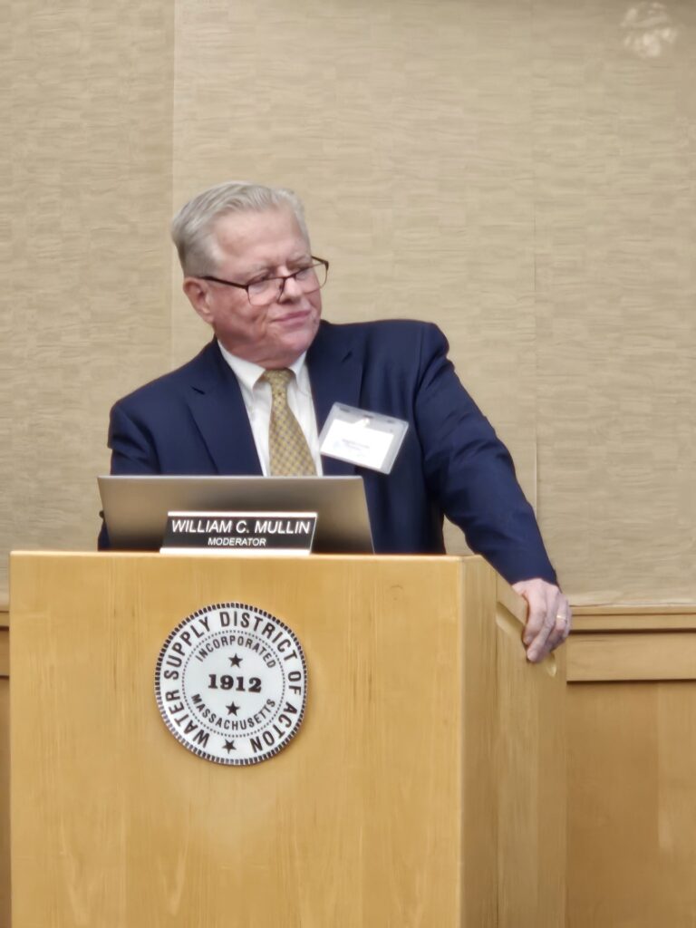A man stands at a podium, looking to his left (towards the Commissioners and other Water District members). He is looking, at best, frustrated.
