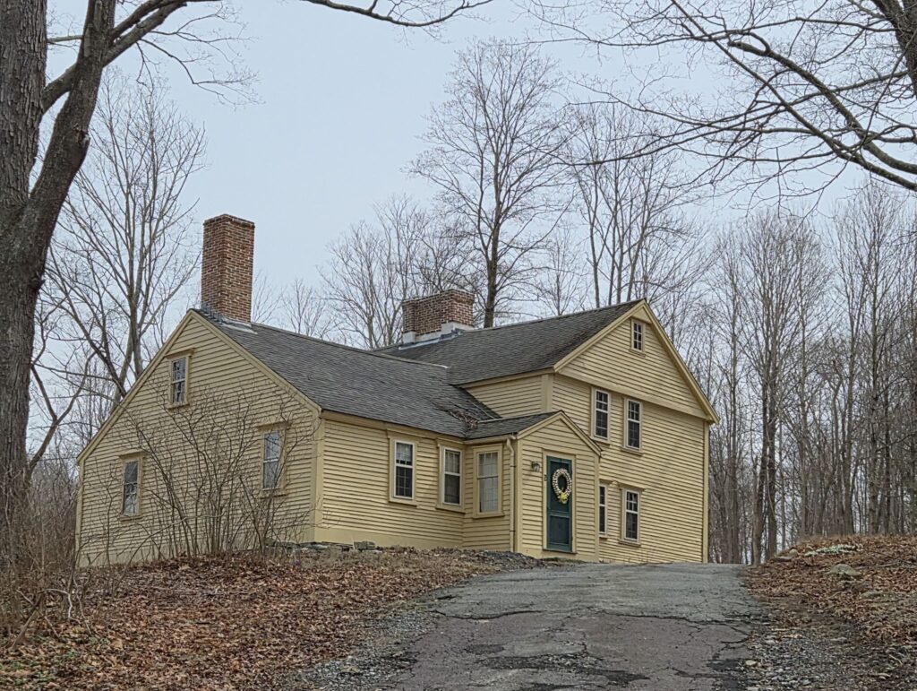 An old (ca 1707) yellow house sits on top of a hill. A shiny wreath hangs from a green door.